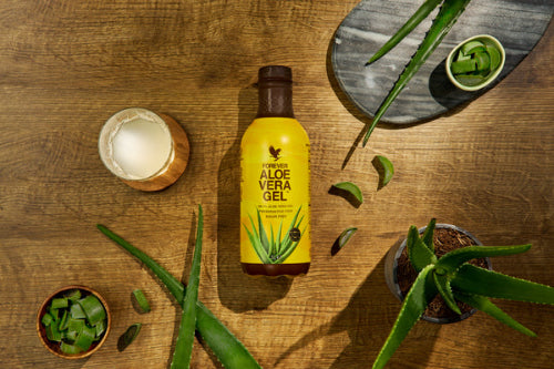 Forever Aloe Vera Gel bottle on a wooden table with aloe vera leaves and a candle.